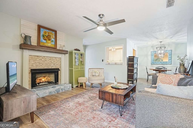 living area featuring visible vents, ceiling fan with notable chandelier, wood finished floors, a fireplace, and baseboards