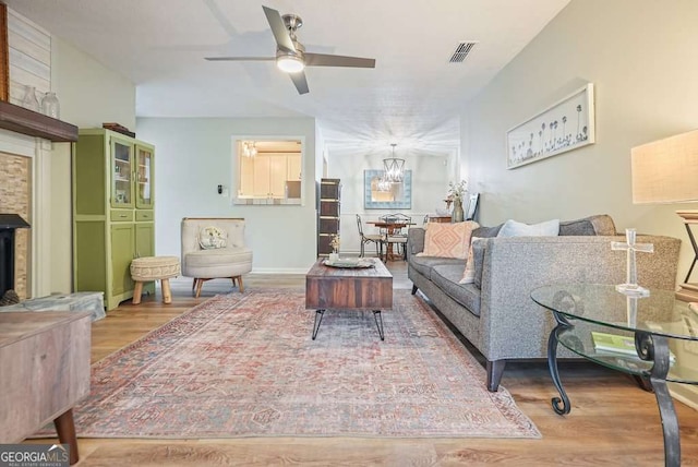 living area featuring visible vents, a fireplace with raised hearth, wood finished floors, and ceiling fan with notable chandelier