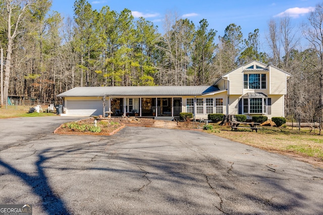 view of front of property featuring fence, driveway, an attached garage, covered porch, and metal roof