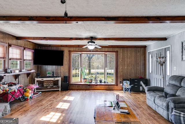 living room with beam ceiling, wood walls, a textured ceiling, and wood-type flooring