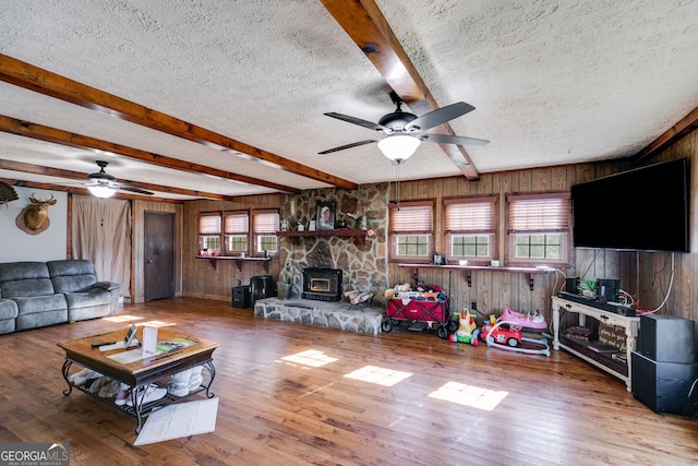 living area featuring wooden walls, beamed ceiling, a wood stove, wood finished floors, and a textured ceiling