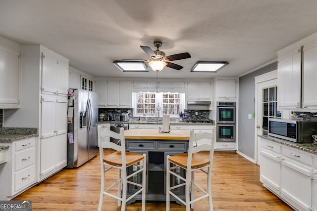 kitchen with light wood finished floors, decorative backsplash, under cabinet range hood, appliances with stainless steel finishes, and white cabinetry