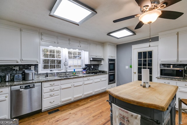 kitchen featuring light wood-style flooring, a sink, appliances with stainless steel finishes, white cabinetry, and tasteful backsplash