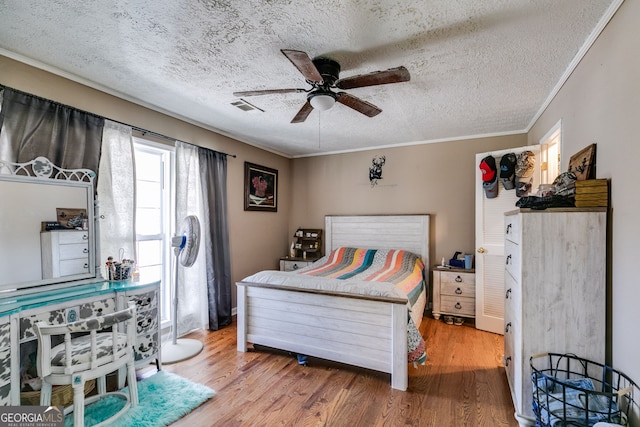 bedroom featuring a textured ceiling, wood finished floors, visible vents, and ornamental molding