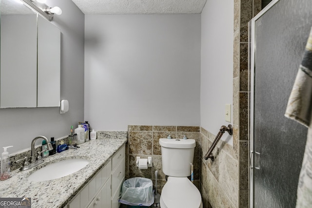 full bath featuring toilet, a textured ceiling, tile walls, a shower stall, and vanity