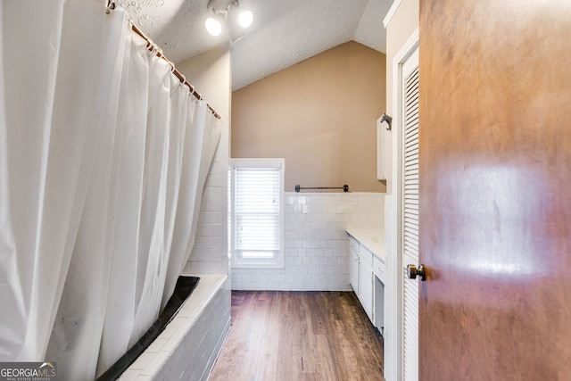 full bathroom featuring a textured ceiling, wood finished floors, a tile shower, tile walls, and vaulted ceiling