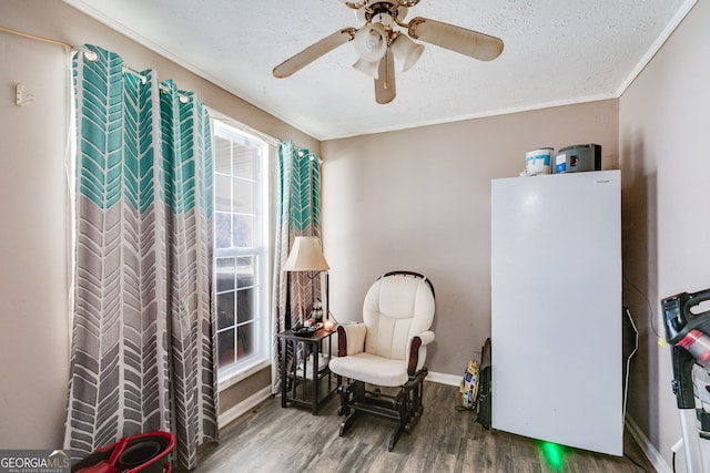 living area with ornamental molding, wood finished floors, baseboards, and a textured ceiling