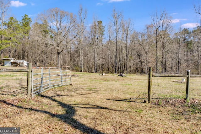 view of yard with a gate, a rural view, a forest view, and fence