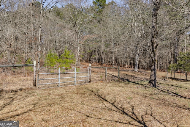 view of yard featuring a gate, a wooded view, and fence