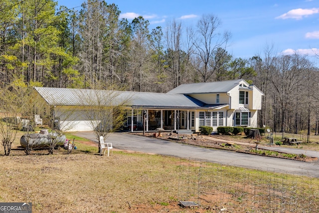 traditional home with aphalt driveway, an attached garage, metal roof, and a view of trees