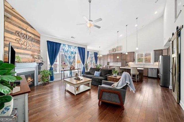 living room featuring visible vents, dark wood-style floors, a glass covered fireplace, high vaulted ceiling, and a ceiling fan