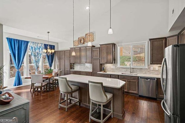 kitchen with a kitchen island, a sink, light countertops, dark wood-type flooring, and appliances with stainless steel finishes