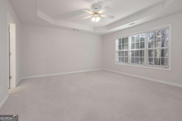 empty room featuring a raised ceiling, baseboards, visible vents, and light carpet