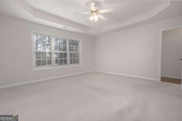 carpeted empty room featuring visible vents, baseboards, a tray ceiling, and a ceiling fan