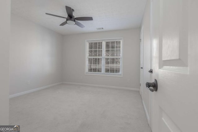 spare room featuring visible vents, light colored carpet, baseboards, and ceiling fan