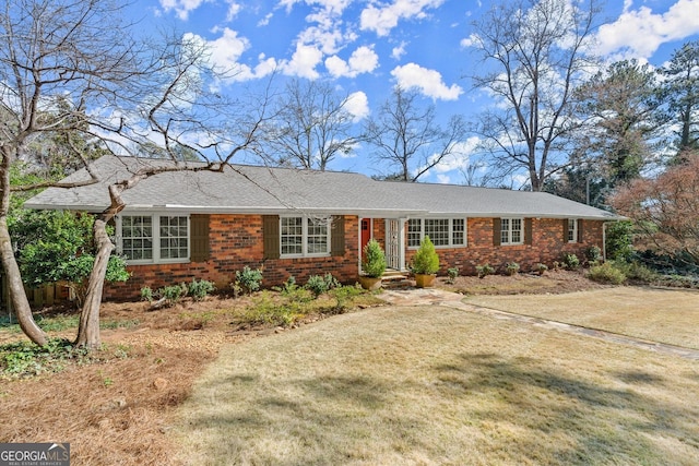 ranch-style home featuring brick siding, a front lawn, and roof with shingles