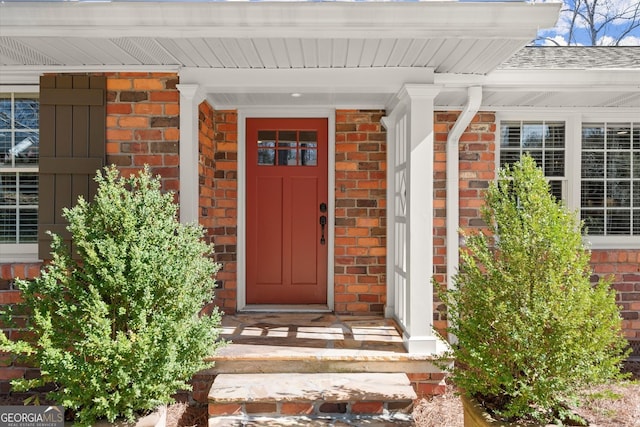 view of exterior entry with brick siding and a shingled roof