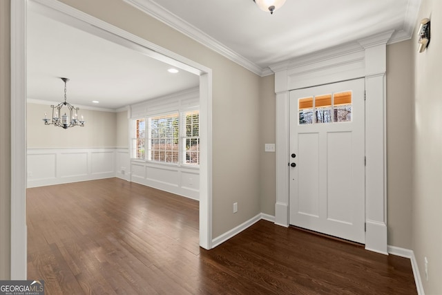 entrance foyer with a wainscoted wall, dark wood finished floors, crown molding, a decorative wall, and a chandelier