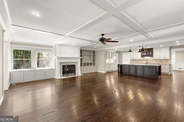 unfurnished living room with dark wood finished floors, beamed ceiling, a glass covered fireplace, coffered ceiling, and a ceiling fan