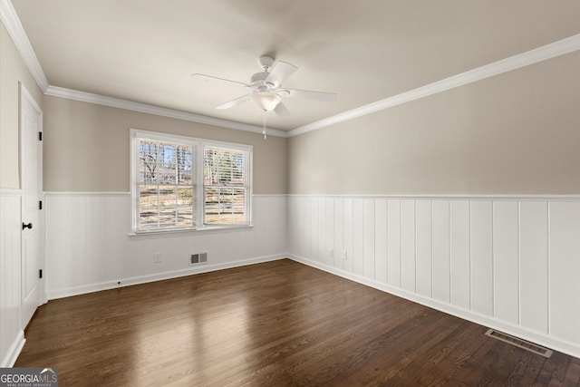 empty room with a wainscoted wall, wood finished floors, visible vents, and ceiling fan