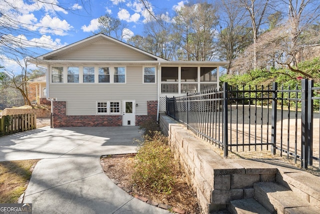 view of front of house featuring brick siding, fence private yard, and a sunroom