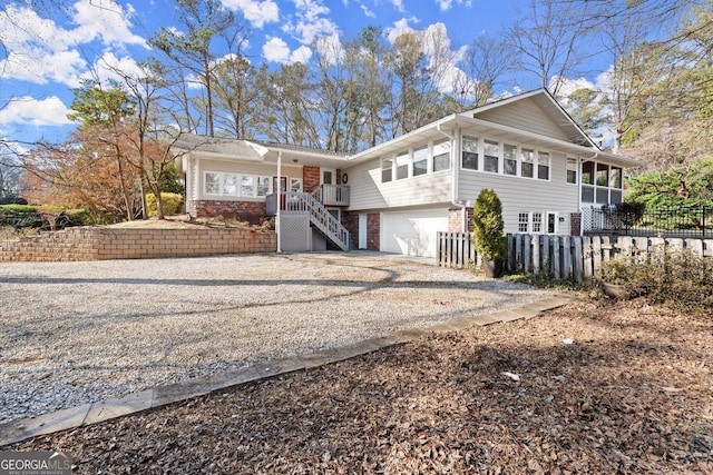 view of front of property with fence, gravel driveway, an attached garage, brick siding, and stairs