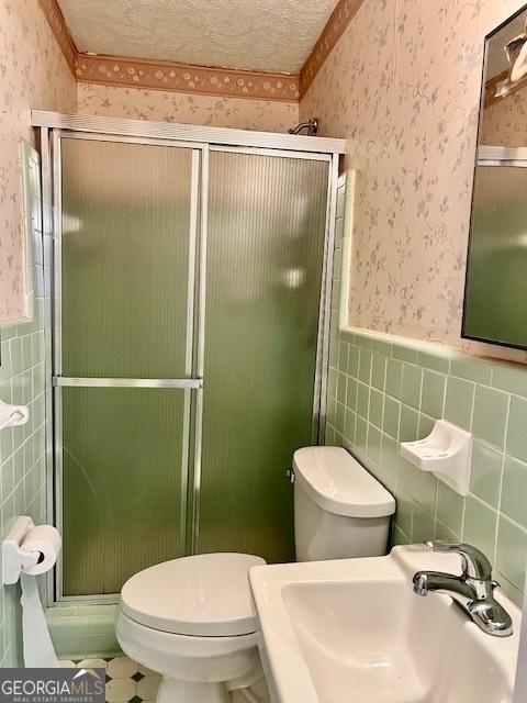 bathroom with wallpapered walls, a textured ceiling, a sink, and wainscoting