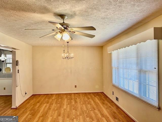 spare room with visible vents, baseboards, wood finished floors, and ceiling fan with notable chandelier