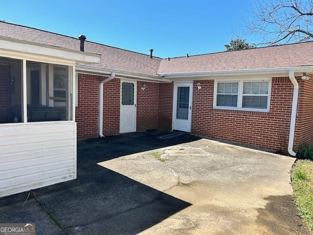 property entrance with a patio, brick siding, and roof with shingles