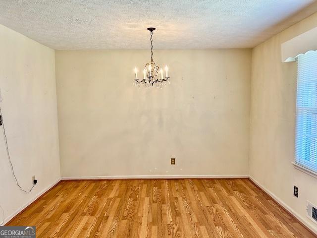 unfurnished dining area with a textured ceiling, baseboards, light wood finished floors, and a chandelier