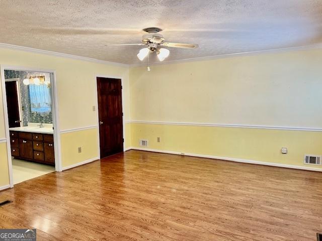 interior space with visible vents, a textured ceiling, light wood-type flooring, and ornamental molding