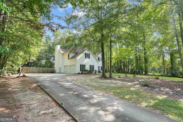 view of property exterior with fence, a garage, driveway, and a chimney