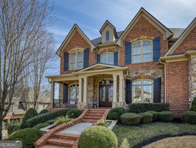 view of front of home featuring brick siding, stone siding, covered porch, and french doors