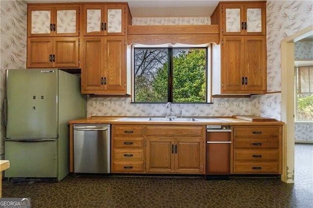 kitchen with a wealth of natural light, a sink, stainless steel dishwasher, freestanding refrigerator, and wallpapered walls