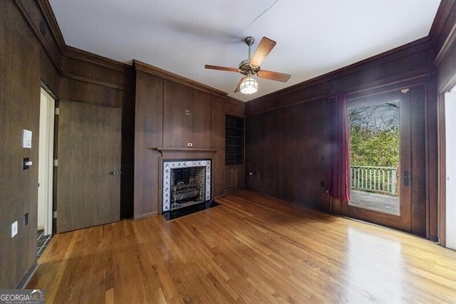 unfurnished living room featuring a fireplace with flush hearth, light wood-style flooring, crown molding, and wood walls