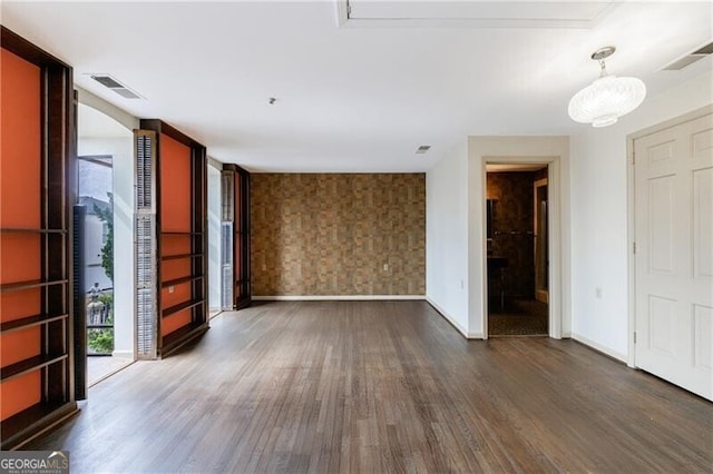 empty room featuring visible vents, baseboards, wood finished floors, and wallpapered walls