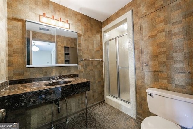 bathroom featuring toilet, a stall shower, tile walls, and a sink