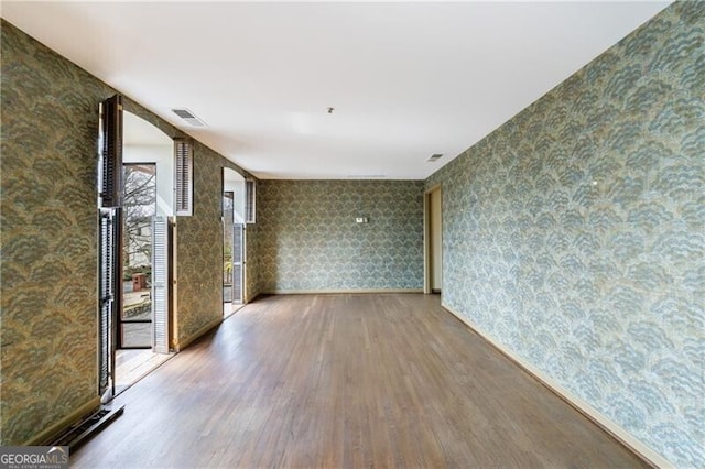 spare room with wallpapered walls, wood finished floors, and visible vents