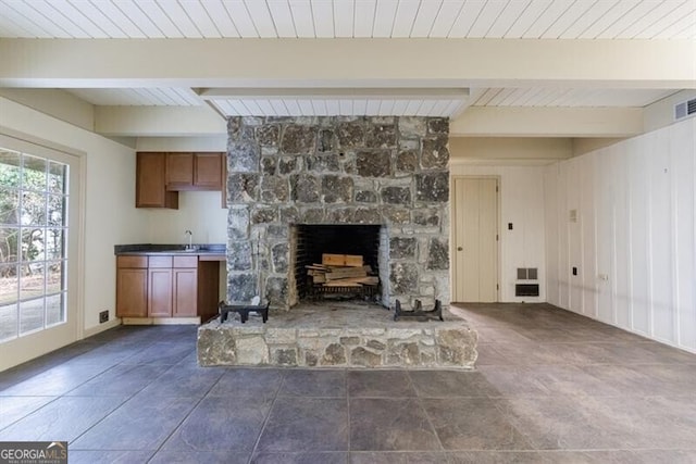 unfurnished living room featuring visible vents, beamed ceiling, a stone fireplace, wooden ceiling, and a sink