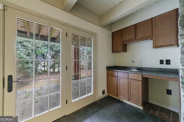 kitchen featuring brown cabinets, dark tile patterned floors, a sink, dark countertops, and baseboards