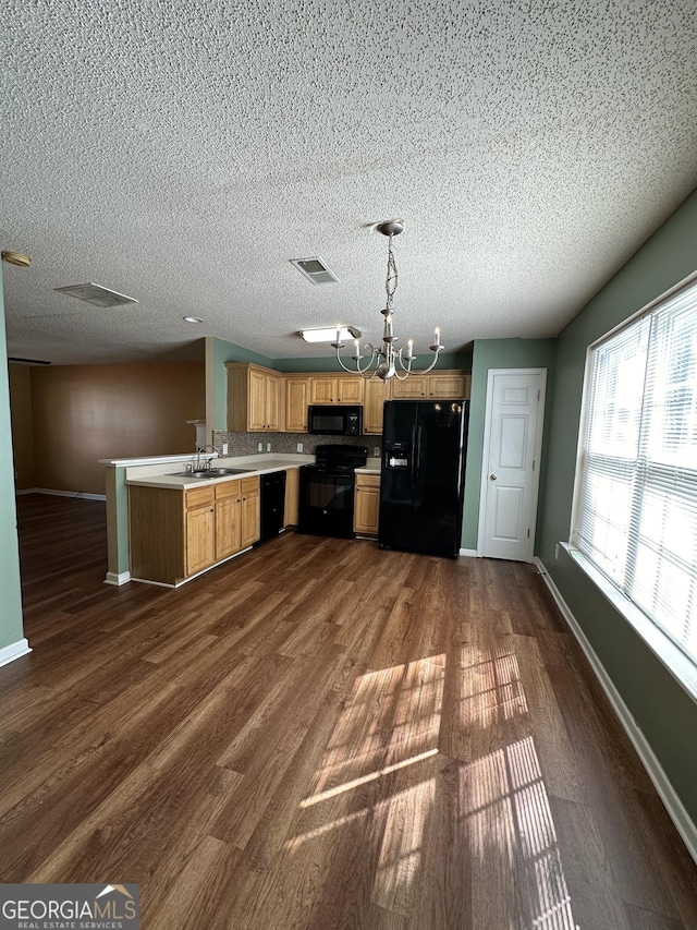 kitchen with black appliances, a sink, a peninsula, light countertops, and dark wood-style flooring