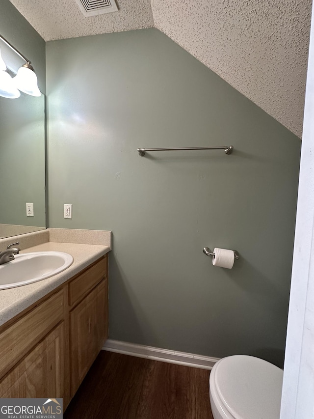 bathroom featuring baseboards, toilet, vaulted ceiling, wood finished floors, and vanity