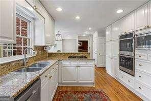 kitchen with dark wood-style floors, a peninsula, a sink, stainless steel appliances, and white cabinets