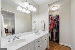 full bathroom with vanity, a walk in closet, baseboards, and wood finished floors