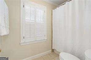 bathroom featuring tile patterned flooring, curtained shower, toilet, and baseboards