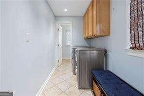 washroom with washer and dryer, light tile patterned flooring, cabinet space, and baseboards