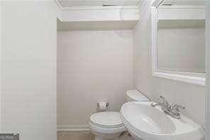 bathroom featuring toilet, crown molding, baseboards, and a sink