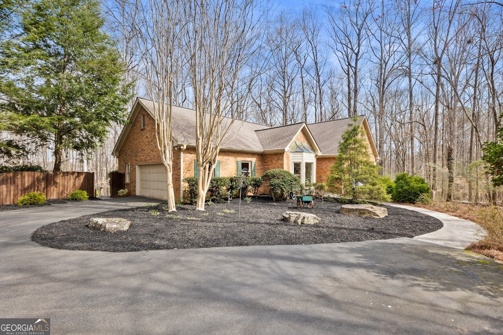 view of front of home with brick siding, fence, roof with shingles, a garage, and driveway