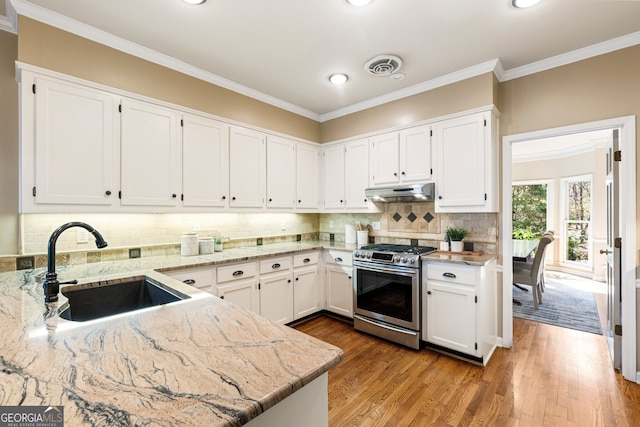 kitchen with visible vents, under cabinet range hood, stainless steel range with gas stovetop, white cabinetry, and a sink