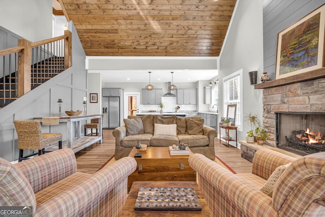 living room with stairway, light wood finished floors, high vaulted ceiling, a stone fireplace, and wooden ceiling